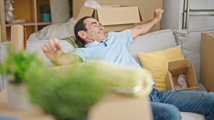 Middle age man sitting on sofa stretching arms at new home