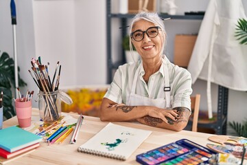 Middle age grey-haired woman artist smiling confident sitting with arms crossed gesture at art studio