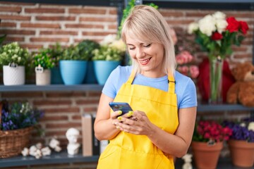 Young blonde woman florist smiling confident using smartphone at florist