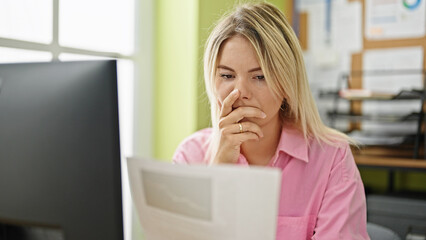 Young blonde woman business worker using computer reading document looking upset at office