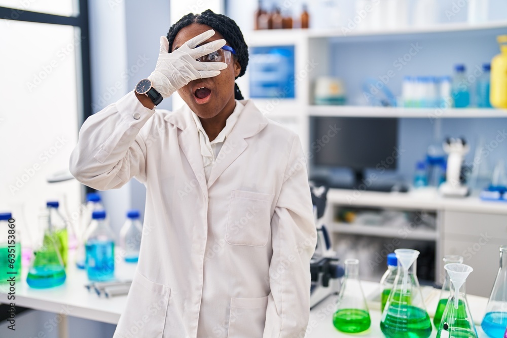 Canvas Prints African american woman working at scientist laboratory peeking in shock covering face and eyes with hand, looking through fingers afraid