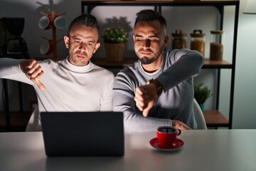 Homosexual couple using computer laptop looking unhappy and angry showing rejection and negative...