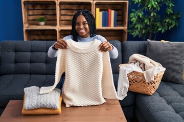 African american woman folding clean laundry winking looking at the camera with sexy expression,...