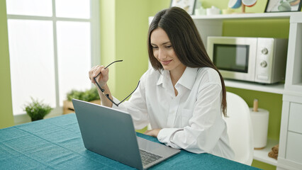 Young beautiful hispanic woman using laptop sitting on table at dinning room