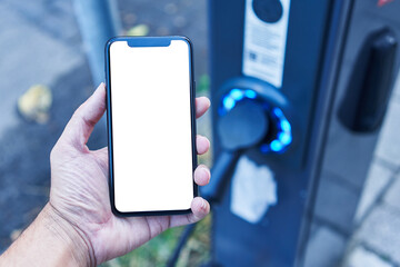 Man holding smartphone showing white blank screen at electrical car station