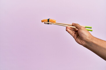  Hand of man holding omelette nigiri with chopsticks over isolated pink background