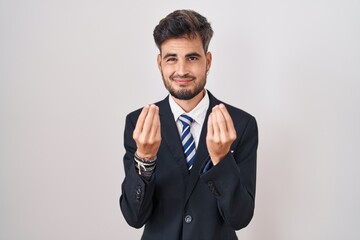 Young hispanic man with tattoos wearing business suit and tie doing money gesture with hands, asking for salary payment, millionaire business