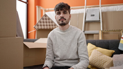 Fototapeta premium Young hispanic man sitting on the sofa serious at new home