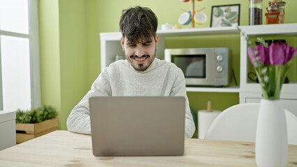 Young hispanic man using laptop at dinning room