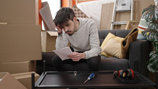 Young hispanic man assembling new table looking at instruction paper at new home