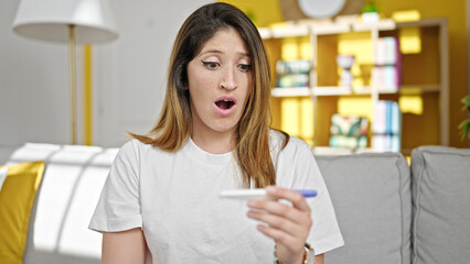 Young blonde woman holding pregnancy test with worried expression at home