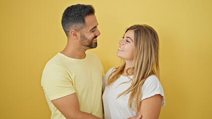 Fototapeta premium Man and woman couple smiling confident hugging and looking each other over isolated yellow background