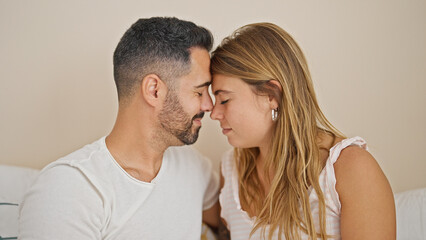 Man and woman couple sitting on bed with heads together at bedroom
