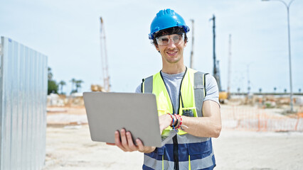 Young hispanic man architect smiling confident using laptop at construction place