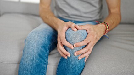 Young hispanic man sitting on sofa suffering for knee injury at home