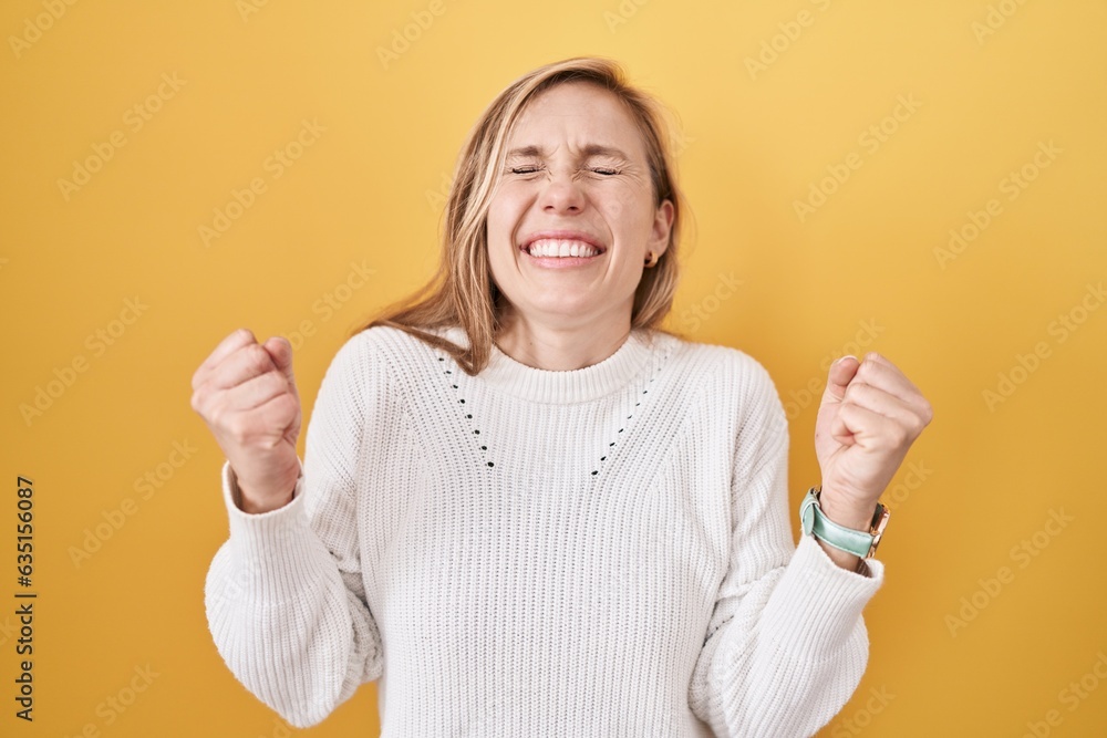 Sticker Young caucasian woman wearing white sweater over yellow background celebrating surprised and amazed for success with arms raised and eyes closed. winner concept.