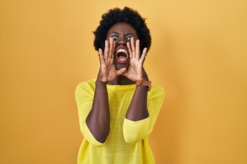 African young woman standing over yellow studio shouting angry out loud with hands over mouth