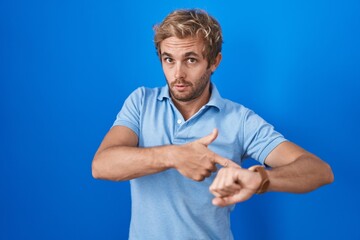 Caucasian man standing over blue background in hurry pointing to watch time, impatience, upset and...