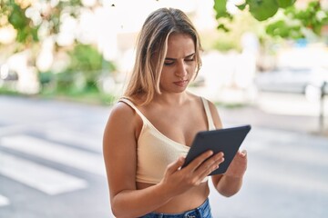 Fototapeta premium Young blonde woman using touchpad with serious expression at street