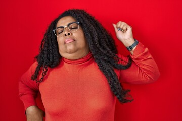 Plus size hispanic woman standing over red background stretching back, tired and relaxed, sleepy and yawning for early morning - obrazy, fototapety, plakaty