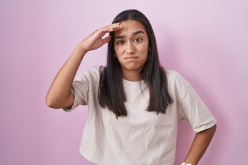 Young hispanic woman standing over pink background worried and stressed about a problem with hand on forehead, nervous and anxious for crisis