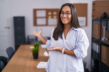 Plakat Young hispanic woman at the office inviting to enter smiling natural with open hand
