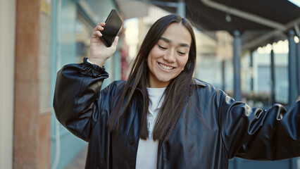 Young beautiful hispanic woman smiling confident using smartphone dancing at coffee shop terrace
