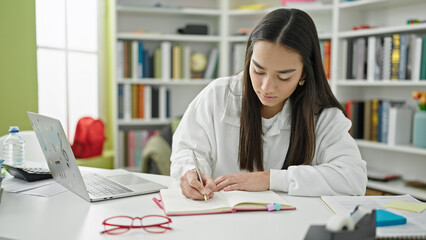 Young beautiful hispanic woman student using laptop writing notes at university classroom