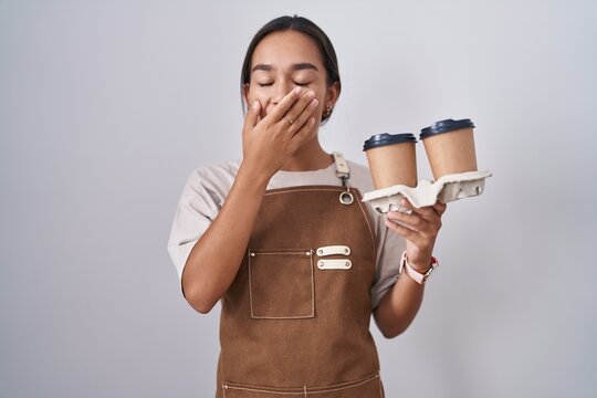 Young hispanic woman wearing professional waitress apron holding coffee bored yawning tired covering mouth with hand. restless and sleepiness.