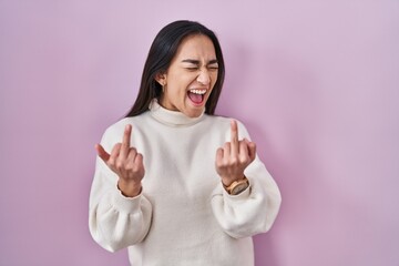 Young south asian woman standing over pink background showing middle finger doing fuck you bad expression, provocation and rude attitude. screaming excited