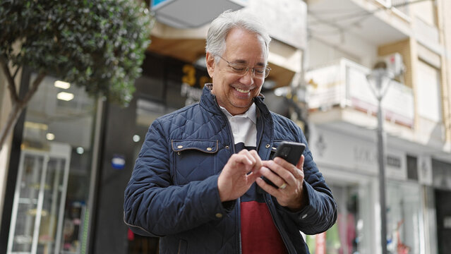 Middle age man with grey hair using smartphone smiling at street
