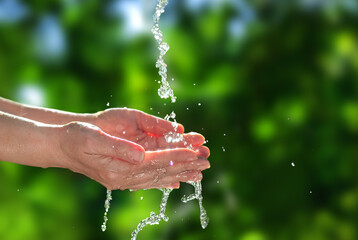 Stream of water on female hands in summertime. Hands with water on natural background for eco...