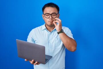 Chinese young man using computer laptop mouth and lips shut as zip with fingers. secret and silent,...