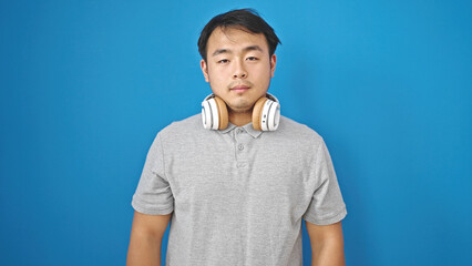  standing with serious expression wearing headphones over isolated blue background