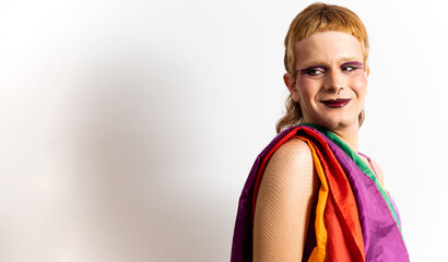 A red-haired non-binary person poses on a white background with an LGBT flag resting on his shoulder while looking sideways. Concept of support for the LGBTI collective, pride for the LGBT collective.