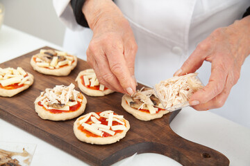 Obraz na płótnie Canvas Adding toppings to the mini pizzas. Adding chicken. Delicious homemade mini pizzas preparation.