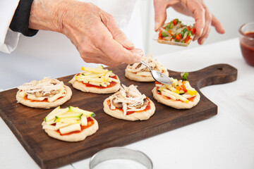 Adding toppings to the mini pizzas. Adding vegetables. Delicious homemade mini pizzas preparation.