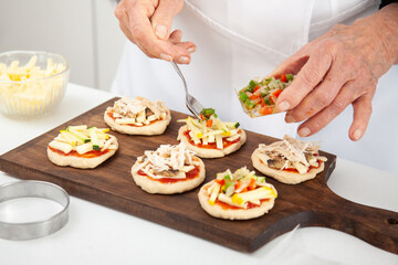 Adding toppings to the mini pizzas. Adding vegetables. Delicious homemade mini pizzas preparation.