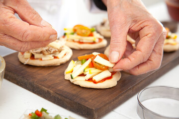 Obraz na płótnie Canvas Adding toppings to the mini pizzas. Delicious homemade mini pizzas preparation.