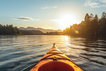 Front of an orange kayak on a lake at sunset. The kayak is pointed towards the horizon and the sun is setting behind the mountains in the background, golden glow - obrazy, fototapety, plakaty