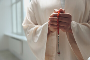 Muslim man with misbaha praying indoors, closeup