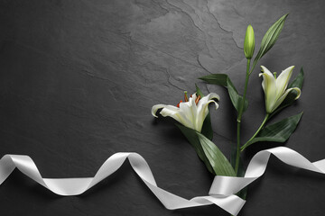 White lilies and ribbon on black table, flat lay with space for text. Funeral symbols