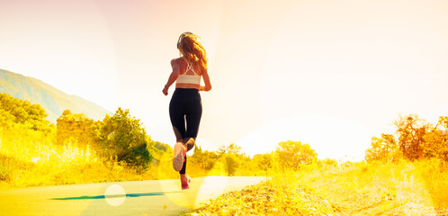 Dynamic woman wearing activewear and listening music with headphones running in nature on morning-...