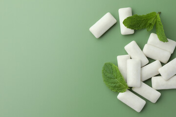 Tasty white chewing gums and mint leaves on light green background, flat lay. Space for text
