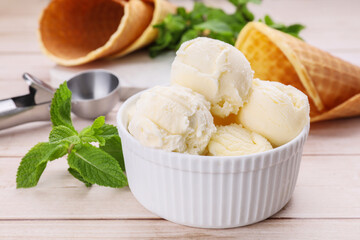 Bowl of ice cream and mint leaves on light wooden table, closeup