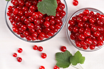 Many ripe red currants and leaves on white wooden table, flat lay