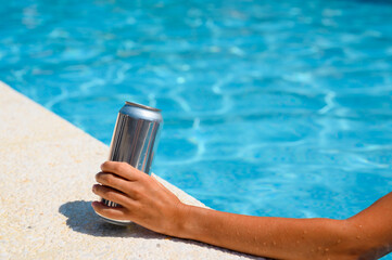 An aluminum can of beer in the hand of a relaxing hotel pool. selective focus on beer. Summer...