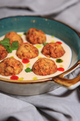 fishballs in white sauce with drops of mint oil and sriracha on a grey steel plate with a grey tablecloth