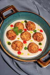 fishballs in white sauce with drops of mint oil and sriracha on a grey steel plate with a grey tablecloth