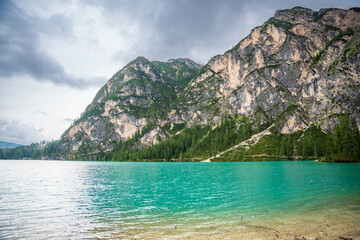 Braies lake surrounded by pine forests and the rocky ranges of the Dolomites in cloudy day, Italy.